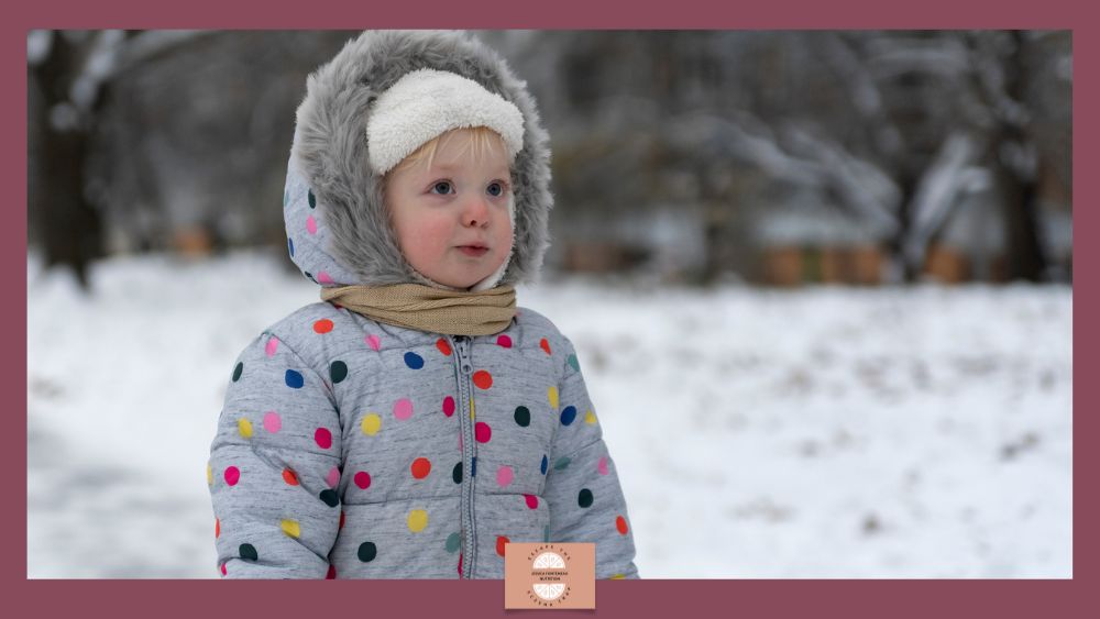 Why Winter Makes Your Child's Eczema Worse - image of a child in a spotted snowsuit, hat and scarf, looking cold in a wintery area.